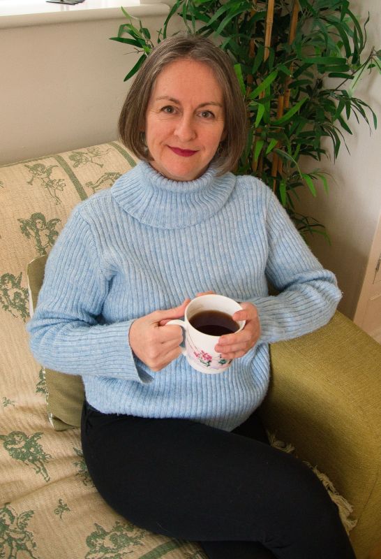 Emma in a blue poloneck with a cup of tea